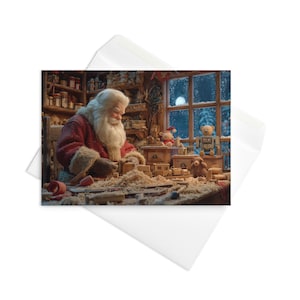 May include: A Christmas card featuring Santa Claus in his workshop, crafting wooden toys. The scene is filled with tools, wood shavings, and finished toys, with a snowy window in the background. The card is inside a white envelope.