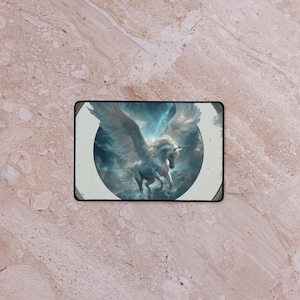 Peut inclure: Tapis de souris rectangulaire avec un Pégase blanc majestueux aux ailes déployées, sur fond de nuages bleus et blancs tourbillonnants. Le motif est encadré d'une bordure noire.