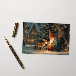 May include: A Christmas-themed postcard featuring a gnome in a red hat and green cloak, sitting with a deer in a snowy forest. The background shows a village with lit windows and a decorated Christmas tree. A black and gold pen is on the left.