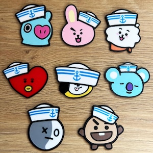 May include: A collection of nine colorful cartoon character patches. Each patch features a different character wearing a sailor hat with a blue anchor design. The characters have various shapes and colors, including blue, pink, red, and white.