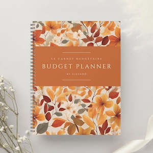 Peut inclure: Un planificateur budgétaire à spirales avec un motif floral dans les tons orange, jaune et marron. La couverture porte l'inscription "Budget Planner" et "Le Carnet Budgétaire" dans un bloc orange rectangulaire. Le planificateur est de Giuyado.