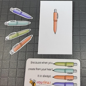 May include: A collection of colorful pen stickers and a single pen illustration on a white card. The stickers include pens in purple, teal, green, and orange. A rectangular sticker features the text "Because when you create from your heart it is always... YOU-TIFUL!"