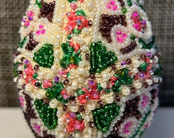 May include: A white egg decorated with pink, green and brown beads in a geometric pattern.