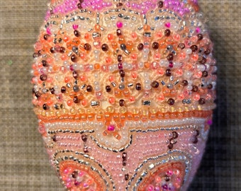 May include: A pink, orange and white beaded Easter egg with a decorative pattern.