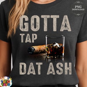May include: Dark gray t-shirt with the text "GOTTA TAP DAT ASH" in a distressed font. The graphic includes a cigar, a glass of whiskey with ice, and a PNG download icon.