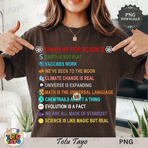 May include: A brown t-shirt with the text "STAND UP FOR SCIENCE" and other science-related statements in various colors. The shirt has a round neckline and short sleeves. The brand name "Totu Tayo" is at the bottom.