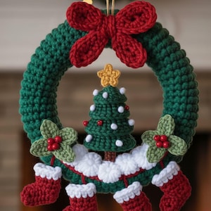 Puede incluir: Una corona navideña hecha a mano con una base verde, adornada con un lazo rojo, un pequeño árbol de Navidad y pequeños calcetines rojos. La corona también presenta hojas de acebo verdes con bayas rojas.