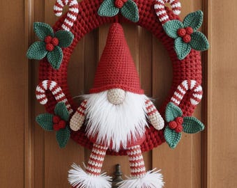 May include: A handmade Christmas wreath with a red crocheted base, green holly leaves, red berries, and candy cane accents. A gnome with a red hat, white beard, and striped legs is the centerpiece. The wreath is suspended on a wooden door.