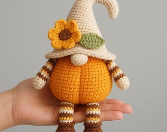May include: A handmade crochet gnome doll with a pumpkin-shaped body. The gnome wears a cream-colored hat adorned with a sunflower and green leaf. Its arms and legs have striped patterns in brown and cream. The gnome is a fall-themed decoration.