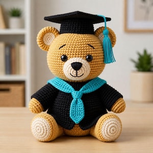 May include: A crocheted teddy bear wearing a graduation cap and gown. The bear is primarily tan with a white muzzle and inner ears. It wears a black cap with a blue tassel and a black gown with a blue collar and tie. The bear is sitting.