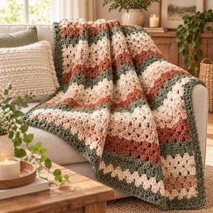 May include: A crocheted throw blanket featuring a repeating granny stripe pattern in alternating horizontal bands of sage green, cream, and terracotta orange, with a solid sage green border framing the entire rectangular textile piece.