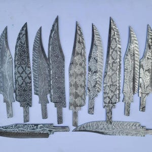 Puede incluir: Una colección de hojas de acero con intrincados patrones grabados. Las hojas varían en forma y tamaño, algunas con diseños florales o geométricos. La colección incluye estilos de hojas puntiagudas y curvas, todas con un brillo metálico.