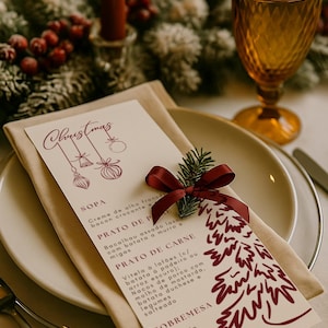 Op de afbeelding: Een feestelijke kerstmenukaart met een bordeauxrode strik en een takje groen, rustend op een gevouwen beige servet en een wit bord. Het menu heeft een kerstboomontwerp en tekst in bordeaux.