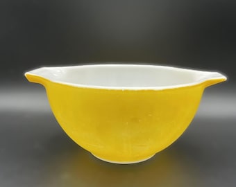 May include: A vintage yellow mixing bowl with a white interior. The bowl has a rounded shape with a flared rim and two small handles. The bowl is made of a durable material and is suitable for kitchen use.