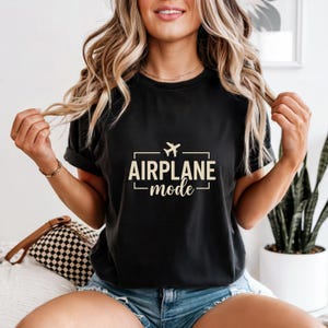 May include: Black t-shirt with the text "AIRPLANE mode" in a rectangular design, featuring a small airplane icon. The shirt is a dark color and has rolled-up sleeves.