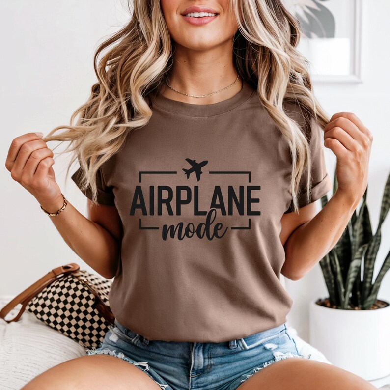 May include: A brown t-shirt with the words "AIRPLANE mode" in black, with a small airplane graphic above the text. The shirt is short-sleeved and appears to be made of a soft material.
