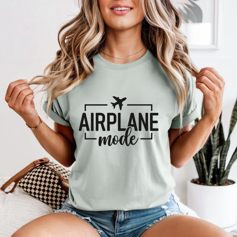 May include: A light green t-shirt with the words "AIRPLANE mode" in black, with a small airplane graphic above the word "AIRPLANE". The t-shirt is a crew neck style.
