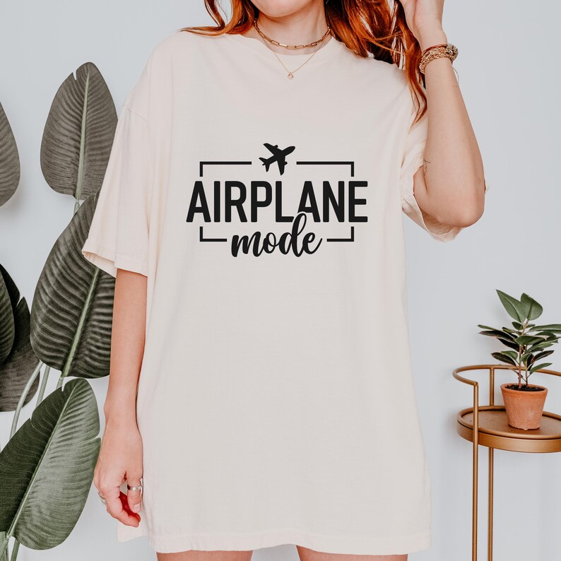 May include: Cream-colored t-shirt with the text "AIRPLANE mode" in black, featuring a small airplane graphic. The shirt has a relaxed fit and short sleeves, suitable for casual wear.