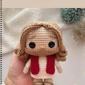 May include: A handmade crochet doll of Jesus, featuring a light brown beard and hair, large black eyes, and a red vest over a white robe. The word "JESUS" is written above the doll.