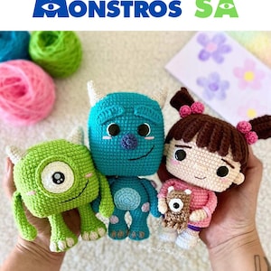 K&ouml;nnte beinhalten: Geh&auml;kelte Monster AG Charaktere: Mike Glotzkowski, Sulley und Boo. Der gr&uuml;ne Mike hat ein Auge, der blaue Sulley hat H&ouml;rner und Boo tr&auml;gt ein rosa Outfit. Das Bild enth&auml;lt den Text "Ebook Monstros SA".