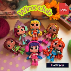 May include: A collection of six handmade crochet dolls, each with unique outfits and hairstyles. The dolls feature vibrant colors like pink, blue, orange, and green. The dolls are arranged on a pink surface, with the text "Winx Club" and "PDF" visible.