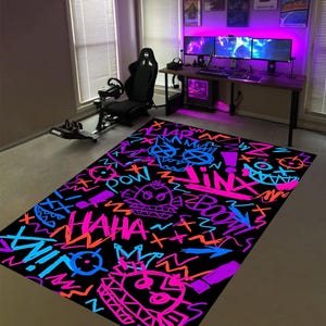 Peut inclure: Tapis rectangulaire noir avec des motifs graffiti néon rose, bleu, orange et violet. Le tapis présente le mot "JINX" et d'autres éléments graphiques. Le tapis est dans une pièce de jeu.