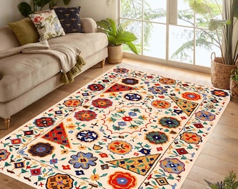 May include: A rectangular ivory rug with a colorful floral and geometric pattern. The rug features a border with red, blue, orange, and yellow shapes. The interior has a repeating pattern of flowers and geometric designs.