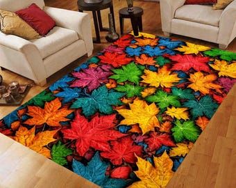 May include: A rectangular area rug featuring a vibrant pattern of colorful autumn leaves. The leaves are in shades of red, orange, yellow, green, blue, and purple. The rug is placed on a wooden floor, with white armchairs and side tables in the background.