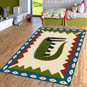 May include: A rectangular area rug with a cartoon alligator design. The rug features a cream-colored background with a green and black alligator. The border is blue with orange eye-shaped designs, and the rug is surrounded by brown and green geometric shapes.