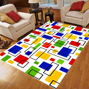 May include: A rectangular area rug with a white background and a colorful geometric pattern. The design features squares and rectangles in red, blue, yellow, and green, outlined in black. The rug is placed on a wooden floor.