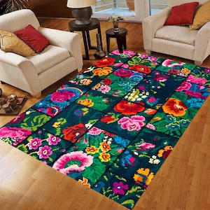 May include: A rectangular rug with a patchwork design. The rug has a dark teal background with vibrant floral patterns in pink, red, orange, yellow, and green. The rug is placed on a wooden floor.