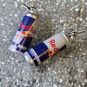 Puede incluir: Un par de pendientes novedosos con forma de mini latas de bebida energ&eacute;tica Red Bull. Las latas son plateadas, blancas y azules con el logotipo y el texto de Red Bull. Los pendientes tienen cierres de gancho de pez plateados.