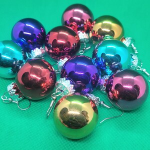 May include: A set of nine colorful Christmas ornament earrings. The ornaments are iridescent and have a metallic finish. The earrings are silver and have a hook closure.