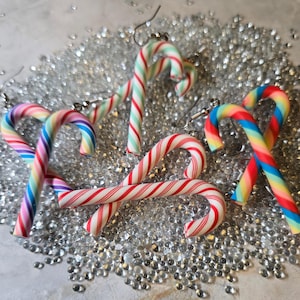 May include: Candy cane earrings in various colors, including red and white stripes, rainbow, and green and white stripes. The earrings are on silver-colored decorative beads.