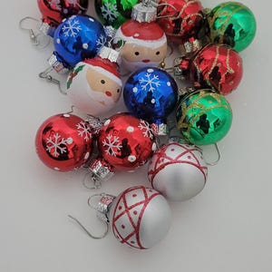 May include: A set of Christmas ornament earrings featuring various designs, including Santa Claus, snowflakes, and glitter. The earrings are made of glass and have silver hooks.