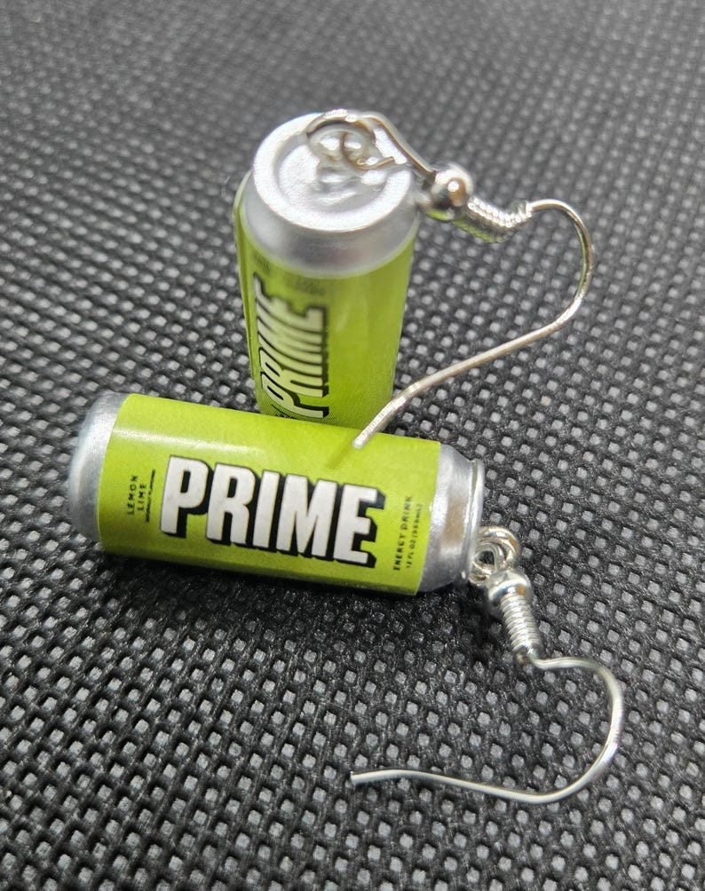 Puede incluir: Un par de pendientes originales con forma de peque&ntilde;as latas de bebida energ&eacute;tica PRIME de color verde lima y plata. Los pendientes muestran la palabra "PRIME" en blanco y las palabras "Lemon Lime" y "Energy Drink". Tienen ganchos plateados.
