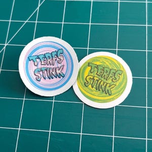 Könnte beinhalten: Ein Set aus drei Keramikbechern mit gesprenkelter, matter Oberfläche. Die Becher sind in Creme-, Hellgrau- und Dunkelgrautönen gehalten. Jeder Becher hat ein schlichtes, minimalistisches Design.