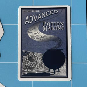 May include: A card with the words "ADVANCED POTION MAKING" in white lettering. The card features a dark blue background with a cauldron and a swirling design. The text "LIBATIUS BORAGE" is at the top.