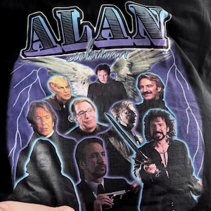 May include: Black t-shirt featuring a graphic of multiple portraits of Alan Rickman, with the name "ALAN" in large, stylized letters above. The design includes a purple and blue color scheme with lightning bolt accents and angel wings.