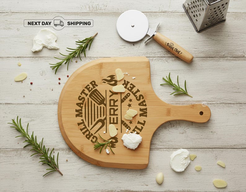 May include: A wooden pizza board with a handle, engraved with "Grill Master Terry". A pizza cutter with a wooden handle and the words "Super Chef" is next to the board. Rosemary sprigs, cheese, and garlic cloves are scattered around the board.