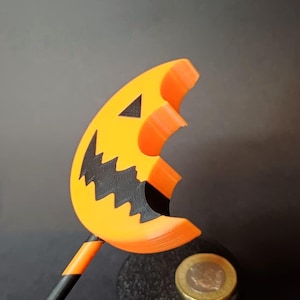 Può includere: Decorazione a tema Halloween con una faccia di zucca arancione e nera stampata in 3D su un bastoncino. La zucca ha una bocca frastagliata e occhi triangolari. Il bastoncino è a strisce nere e arancioni. Una moneta poggia su una base cilindrica nera.