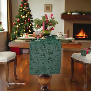 May include: A festive Christmas table setting with a green table runner patterned with gold Christmas trees. The table is set with plates, glasses, and a centerpiece of greenery and red berries. A decorated Christmas tree and fireplace are in the background.