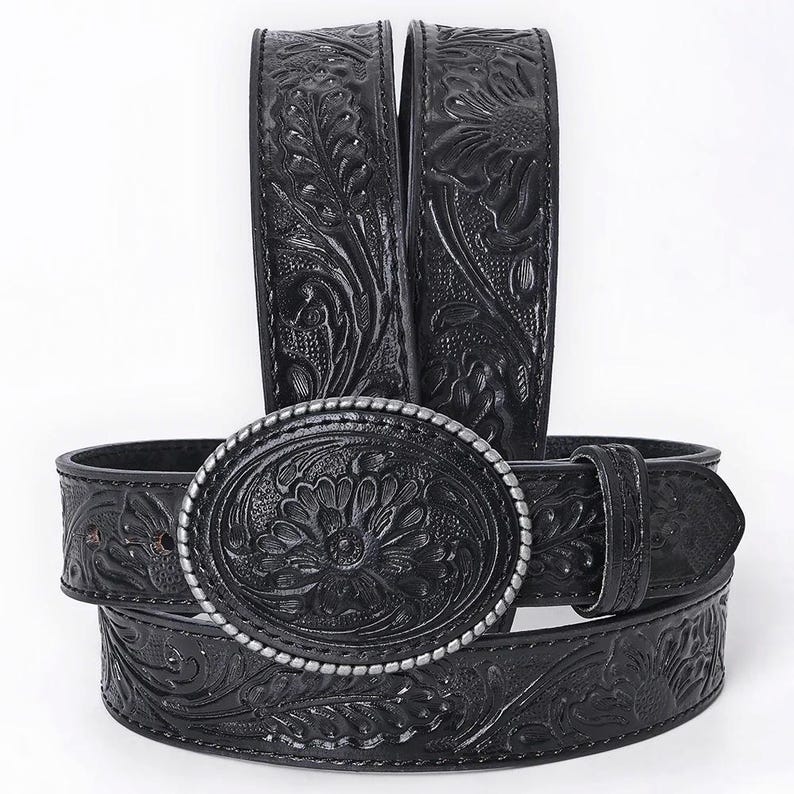 K&ouml;nnte beinhalten: Schwarzer Lederg&uuml;rtel mit gepr&auml;gtem Blumen- und Blattmuster. Die ovale, silberfarbene Schnalle zeigt ein zentrales Blumenmotiv. Das Design des G&uuml;rtels wiederholt sich &uuml;ber die gesamte L&auml;nge und zeigt ein detailliertes, strukturiertes Muster.
