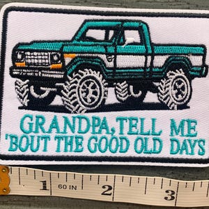 May include: A rectangular embroidered patch featuring a teal and white pickup truck with large tires. Below the truck, the text reads "GRANDPA, TELL ME 'BOUT THE GOOD OLD DAYS" in teal. A measuring tape shows the patch is 3 inches wide.