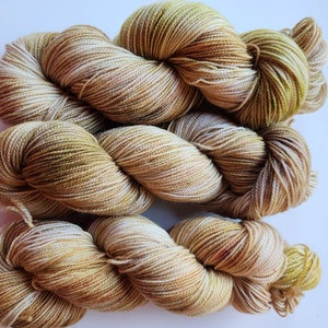 May include: A skein of yarn in shades of beige, brown, and green. The yarn is hand-dyed and has a variegated color pattern.