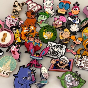 May include: A collection of colorful enamel pins featuring various cartoon characters, including Courage the Cowardly Dog, Dexter, Cosmo, Wanda, and Carl Fredricksen. The pins display diverse shapes, including circular, heart-shaped, and character-specific outlines.
