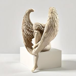 Könnte beinhalten: Beige Engelsstatue mit großen, detaillierten Flügeln, sitzend auf einem weißen Würfel. Der Engel ist mit dem Kopf auf den Knien dargestellt, was eine ruhige und kontemplative Pose ergibt. Die Statue ist ein dekorativer Gegenstand.