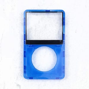 May include: A transparent blue plastic device frame with a rectangular screen area and a circular opening. The top section has a black border. The device is empty, showing the internal structure. The frame is on a white surface.