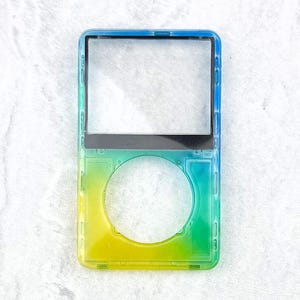 May include: A clear, rectangular case with a gradient of colors, transitioning from yellow to green and blue. The case has a large circular opening and a rectangular opening, likely for a screen. The case is designed to protect a device.
