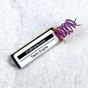 May include: A small, rectangular taptic engine component with the text "iPodmania.com Taptic Engine" printed on a white label. The component has red and blue wires coiled at one end.
